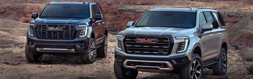 A black and silver 2025 GMC Yukon parked on red dirt terrain near a desert valley under bright daylight.